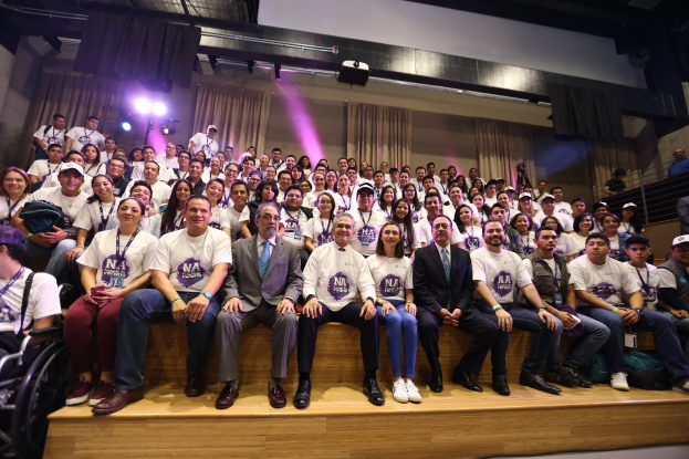 Gruppe von Menschen auf einer Bühne mit einer Person im Rollstuhl links, Vorhänge und Beleuchtung im Hintergrund bei einer NBA-Frauensitzung.