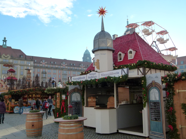Ein pulsierender Weihnachtsmarkt in Nürnberg, Deutschland mit Menschen um geschmückte Stände, festliche Lichter und Schmuck, Gebäude im Hintergrund, ein Riesenrad und ein Schild auf der rechten Seite.