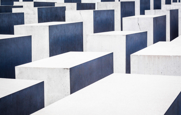 Luftaufnahme des Holocaust-Mahnmals für die ermordeten Juden Europas in Berlin, die zahlreiche weiße und blaue rechteckige Blöcke zeigt, die in einem Gittermuster angeordnet sind.