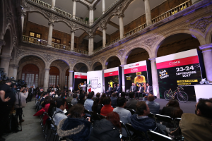 Eine Gruppe von Menschen sitzt an einem Tisch mit einem Podium und einem Mikrofon vor einer Menge, Kameras und Bannern, was auf eine Pressekonferenz für das CDMX 2017-Event hinweist.