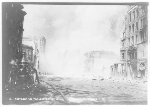 Schwarz-weiß-Foto einer Stadtstraße mit einem Feuerwehrauto auf der linken Seite, Gebäuden auf der rechten Seite und Rauch im Hintergrund, mit Text unten.