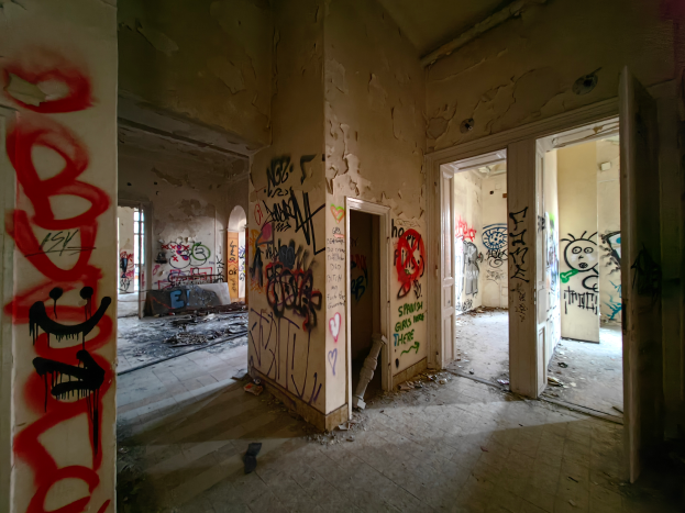 Ein verlassenes Gebäude mit buntem Graffiti an seinen Wänden und Türen, umgeben von verstreuten Gegenständen auf dem Boden, die ein Gefühl von Verfall und Vernachlässigung vermitteln.