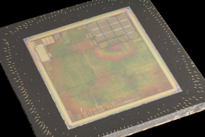 Nahaufnahme eines rechteckigen Halbleiterchips mit metallischem Glanz, schmalem Metallrahmen und kleinen L├Âchern an seinen Kanten, vor schwarzem Hintergrund.