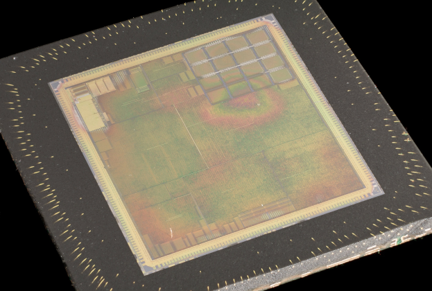 Nahaufnahme eines rechteckigen Halbleiterchips mit metallischem Glanz, schmalem Metallrahmen und kleinen L├Âchern an seinen Kanten, vor schwarzem Hintergrund.