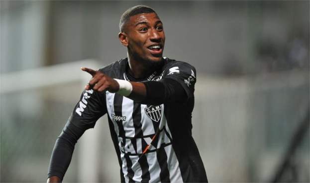 Fußballspieler in einem schwarz-weißen gestreiften Trikot, der lächelt und ein Tor feiert, mit einem unscharfen Hintergrund.