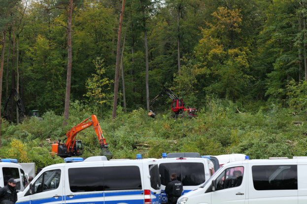 Eine Gruppe von Polizeiwagen in einem waldigen Gebiet geparkt, mit Officers in Mðtzen und Jacken in der Nähe, ein Bagger im Hintergrund und Trees und Himmel öber ihnen.