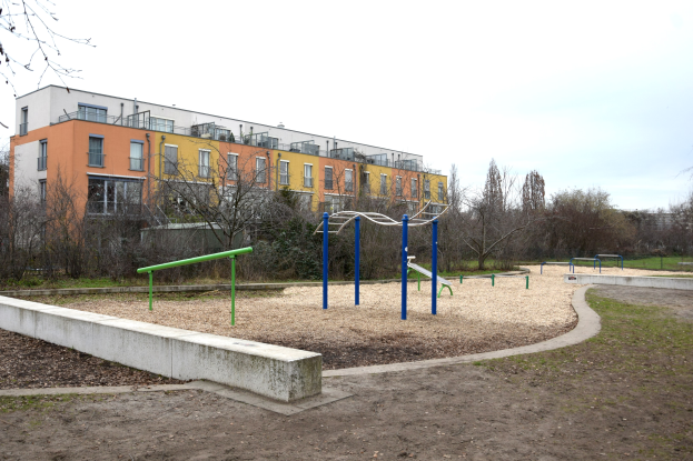 Spielplatz mit einem Gebäude, Bäumen und einem klaren blauen Himmel auf saftig grünem Gras.