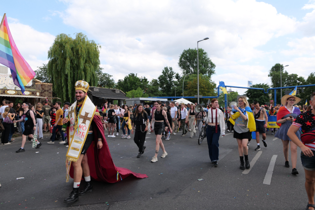 Eine Gruppe von Menschen, die bei der Pride Parade 2018 marschieren und eine Regenbogenflagge sowie Musikinstrumente tragen.