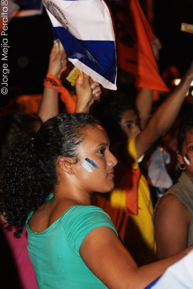 Frauen in grünen T-Shirts bei einer Demonstration mit weißen Schildern, mit mehreren Mädchen im Hintergrund.
