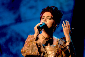 Eine Frau in einem goldenen Kleid singt auf der Bühne des Eurovision Song Contest in ein Mikrofon, mit einem blauen und schwarzen Hintergrund.