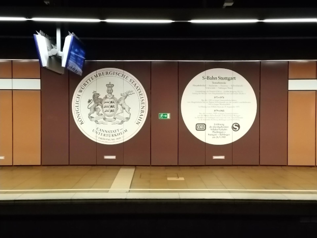 Ein Bahnsteig mit einer 'S-Bahn Stuttgart'-Plakette und Logo an der Wand, Deckenleuchten und einigen Gegenständen auf der linken Seite des Bahnsteigs.