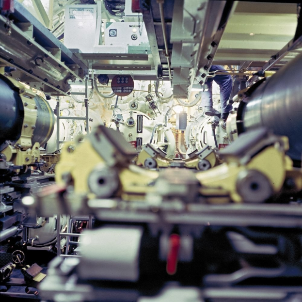 Ein Mann steht auf einer Maschine in einem industriellen Raum, umgeben von Gerät, und scheint Wartungs- oder automatisierungsbezogene Aufgaben durchzuführen.