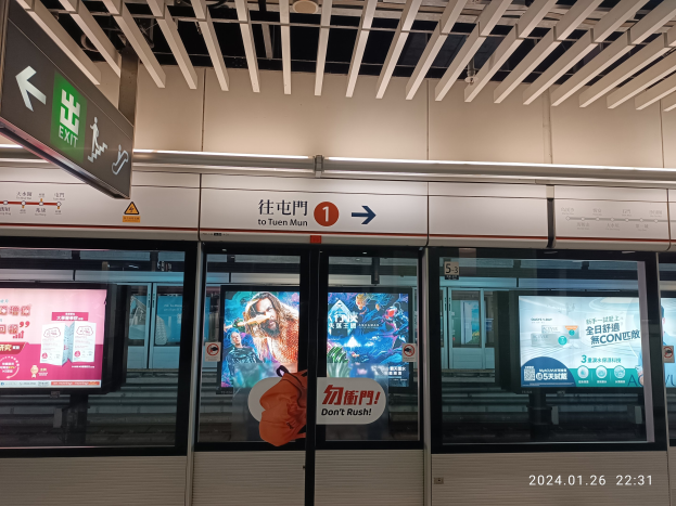 Eine U-Bahn mit Glastüren und digitalen Bildschirmen an einem Bahnhof, mit Text- und Nummernschildern an der Wand und Deckenbeleuchtung.