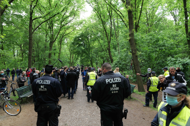 Eine Gruppe von Polizisten vor einer Menschenmenge mit Fahrrädern und einer Bank im Vordergrund und Bäumen im Hintergrund.