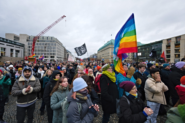 Eine große Gruppe von Menschen mit LGBTQ+-Rechten-Schildern und Fahnen vor einem Gebäude mit einem Kran im Hintergrund.