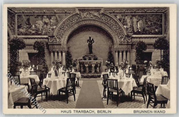 Ein altes Schwarz-Weiß-Foto eines Berliner Restaurants mit Tischen, Stühlen, Blumenvasen und einer Statue im Hintergrund, mit Skulpturen und Pflanzen an den Wänden und Text unten.